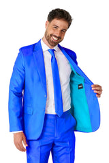 A smiling man in a vibrant Solid Blue suit from Suitmeister reveals the turquoise lining of his open jacket, paired with a white shirt and blue tie.