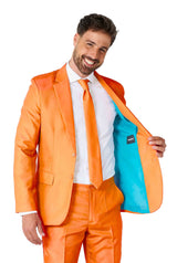 A man grins while wearing the Suitmeister Solid Orange suit, complete with a stylish blue lining that he proudly displays by showcasing the inside of his jacket. He pairs it expertly with a crisp white shirt and an orange tie.