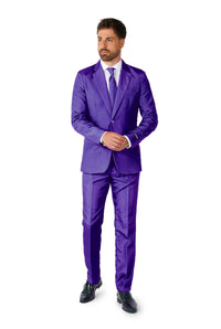 A man in a Suitmeister Solid Purple suit, complete with a white shirt and matching purple tie, stands with his hands clasped. He is wearing dark shoes and looking to the side against a white backdrop.