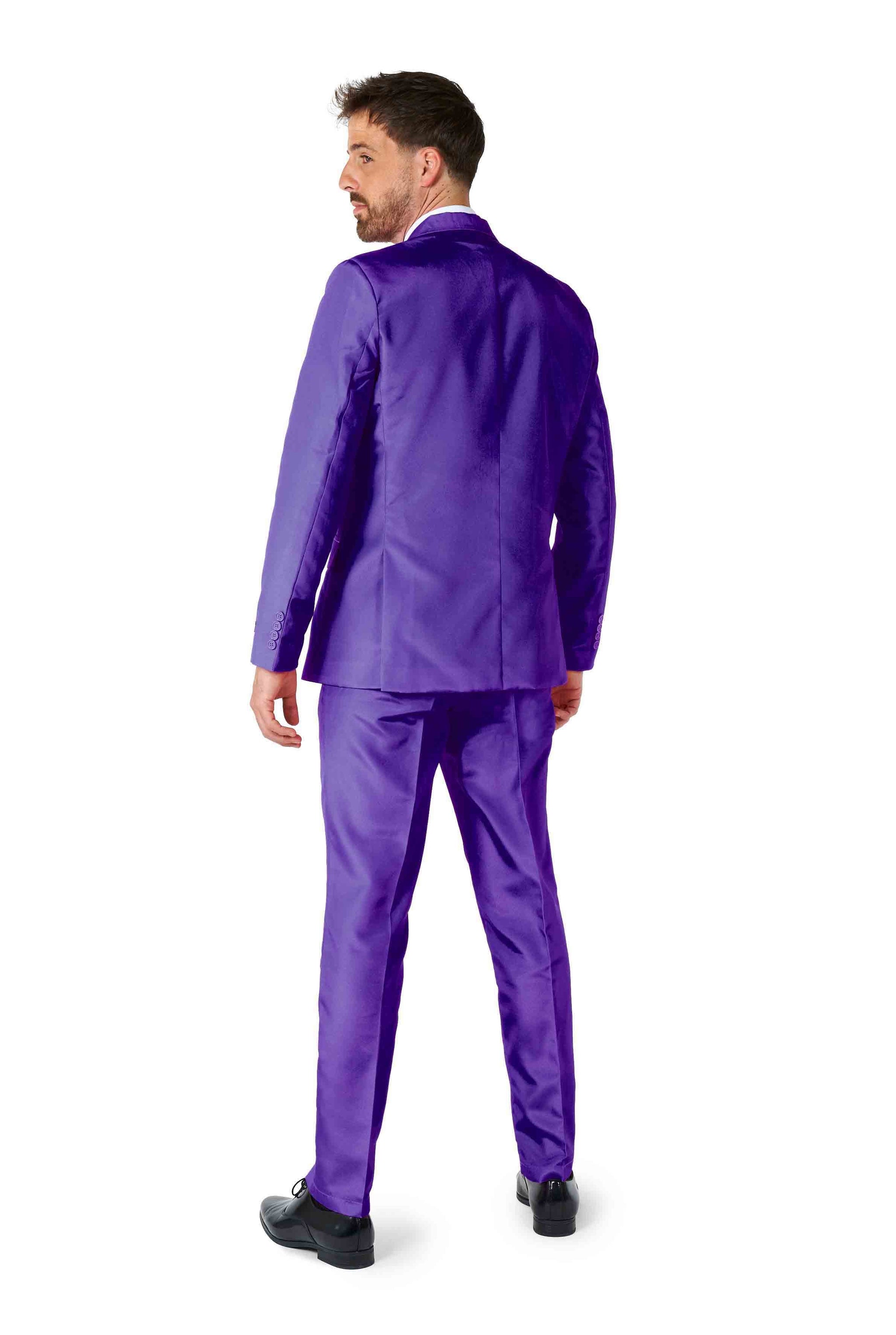 A man dressed in the Suitmeister Solid Purple suit is photographed from behind, glancing over his shoulder. He pairs it with black shoes and has short dark hair, all set against a white background.