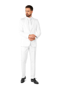 A man stands against a white background dressed in a Suitmeister Solid White suit, complemented by a white shirt and tie. With a beard and hands clasped together, he gazes to the side, finishing off his look with black dress shoes.