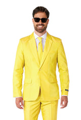 A man donning a vibrant Suitmeister Solid Yellow suit and tie, paired with sunglasses, flashes a smile. He is wearing a white dress shirt beneath and stands against a plain white background.