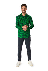 A man wearing the "St. Pats Green" St Patrick's Day shirt by Suitmeister, along with dark pants, stands smiling against a white background. He has short hair and a beard, accessorized with white sneakers. His hands are clasped in front of him.