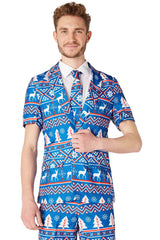 A person is wearing the Suitmeister's "Christmas Blue Nordic" suit, which boasts a festive design with reindeer and Christmas tree patterns in vibrant red, white, and blue colors. The ensemble includes a matching tie against a plain white background.