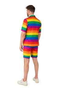 A person stands facing away, wearing the Suitmeister Rainbow suit, which features bright rainbow-striped short sleeves and matching shorts. They have short hair and are wearing white sneakers, set against a plain white background.