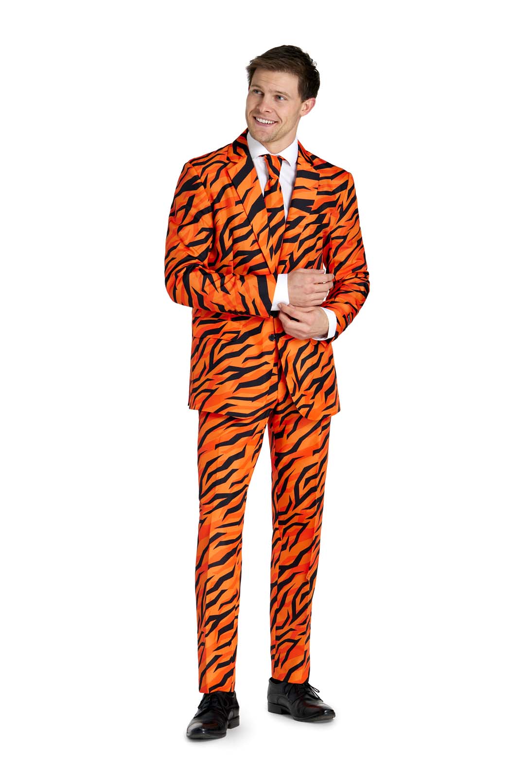 Dressed in the vibrant Tiger suit Orange by Suitmeister, a person stands confidently on a plain white background. The ensemble features bold black tiger stripes against an orange backdrop, complemented by a crisp white shirt and matching tie. As they adjust their sleeve with a smile, their look is completed with sleek black shoes.