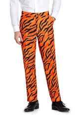 A person is standing with one hand in their pocket, wearing the Suitmeister "Tiger suit Orange," which features bright orange pants with a bold black tiger stripe pattern. They have paired it with a white dress shirt and black shoes.