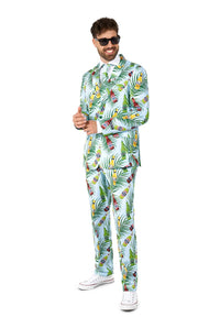 A man is dressed in the vibrant "Tropical Beers Blue - Festival suit" by Suitmeister, featuring a lively print of leaves and flowers. He pairs it with a crisp white shirt and clean white sneakers. With a smile on his face, he completes his look with dark sunglasses, standing against a simple white background.