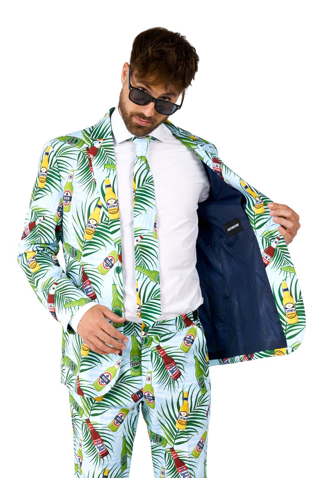 A man clad in the Tropical Beers Blue - Festival suit by Suitmeister, complete with sunglasses, opens the jacket to showcase its inner lining. The ensemble boasts vibrant tropical motifs of pineapples and leaves set against a light background. He poses against a solid white backdrop.