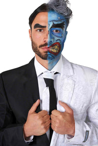 A man is dressed in the Two Face™ suit by Suitmeister, featuring a split design with one side black and white. Half of his face is painted blue with exaggerated features, while the other half remains natural with a neutral expression. He stands against a white background.