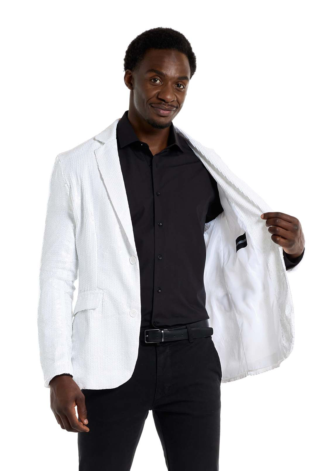 A man is standing, wearing the Suitmeister Sequins Blazer in white over a black shirt and pants. He is holding the blazer open with one hand, smiling against a white background.