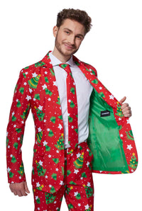 A man is dressed in the Suitmeister Christmas Trees Stars Red - Christmas suit, featuring a festive red jacket adorned with Christmas tree and star patterns. He completes the look with a matching tie and crisp white shirt. Enthusiastically smiling at the camera, he opens one side of his jacket to showcase its vibrant green lining.